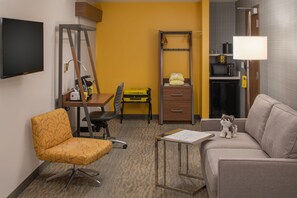 Ein Hotelzimmer mit Schreibtisch, Stuhl, Sofa und einem kleinen Tisch mit Lampe.