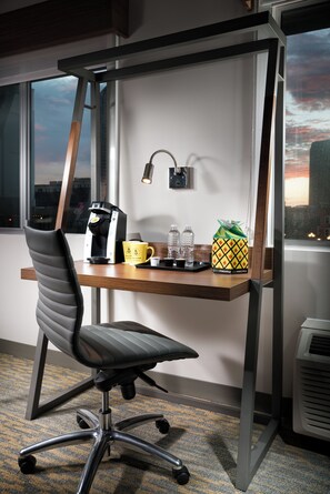 Una silla de oficina moderna con un respaldo alto y estructura metálica, ubicada frente a un escritorio de madera con una cafetera Keurig integrada.