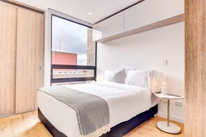 A modern bedroom with a large window, a bed with white bedding, a bedside table with a lamp, and a wooden floor. - w Distinct Loft in the Heart of Bogot (Bogotá)