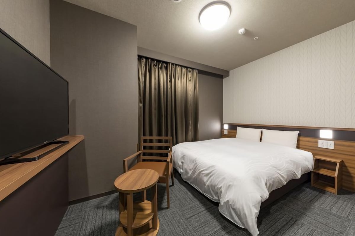 A hotel room with a bed, a desk, a chair, a TV, and a curtain.
