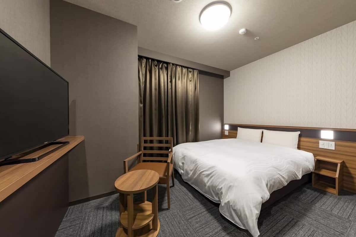 A hotel room with a bed, a desk, a chair, a TV, and a curtain.