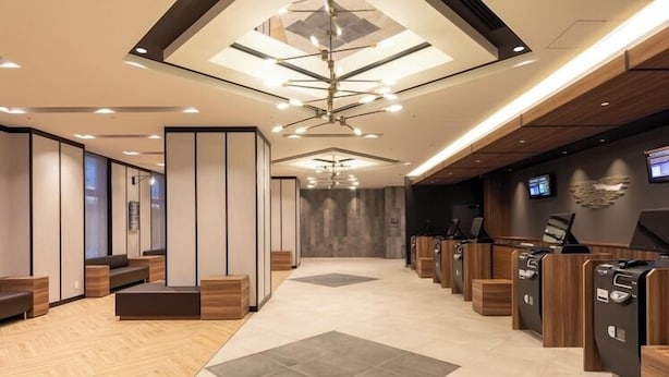A modern hotel lobby with a central seating area, a reception desk, and a large chandelier.
