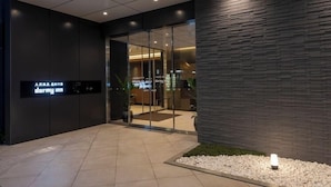 A modern hotel entrance with a dark facade, glass doors, and a sign reading 'dormy inn.'