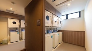 A laundry room with multiple washing machines and dryers, wooden paneling, and a window providing natural light.