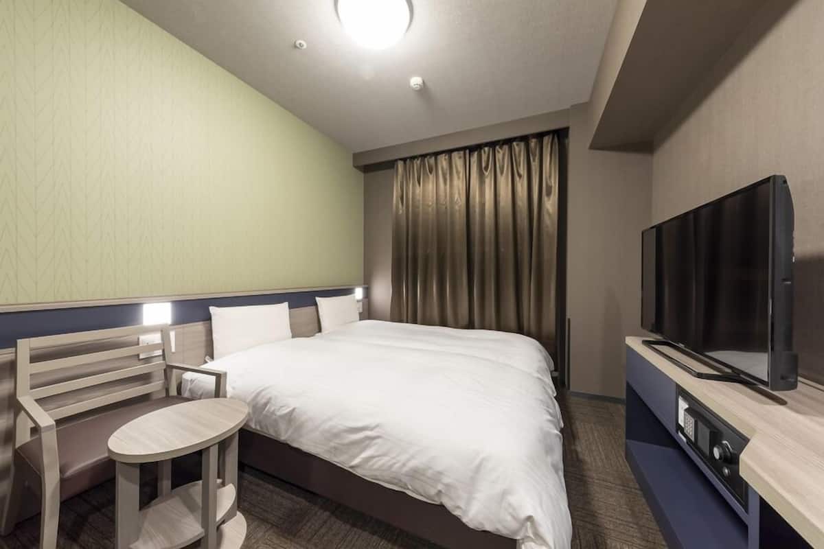 A hotel room with a bed, a TV, a small table, and a bench.