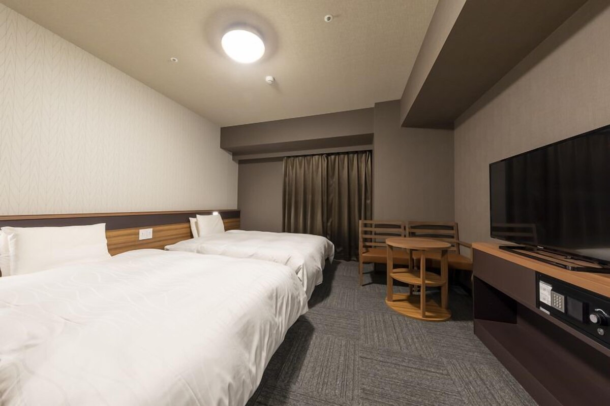 A hotel room with two beds, a TV, a desk, and a chair.