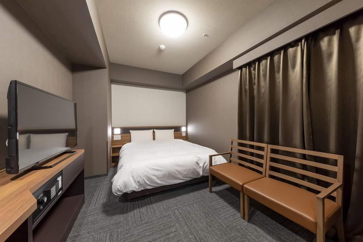 A hotel room with a bed, a TV, a bench, and a curtain.