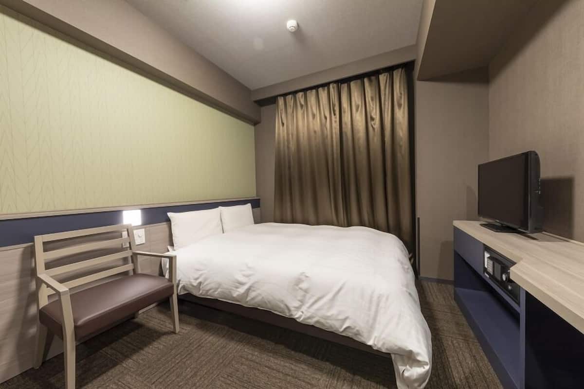 A hotel room with a bed, a TV, a desk, and a bench.
