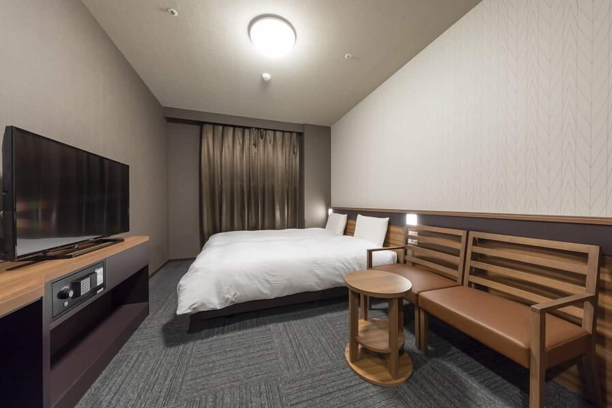A hotel room with a bed, a TV, a wooden bench, and a small round table.