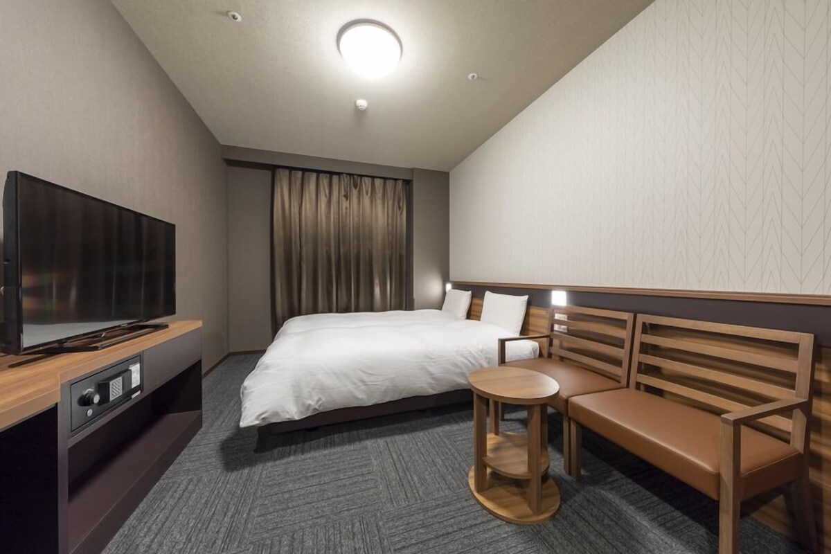 A hotel room with a bed, a TV, a wooden bench, and a small round table.