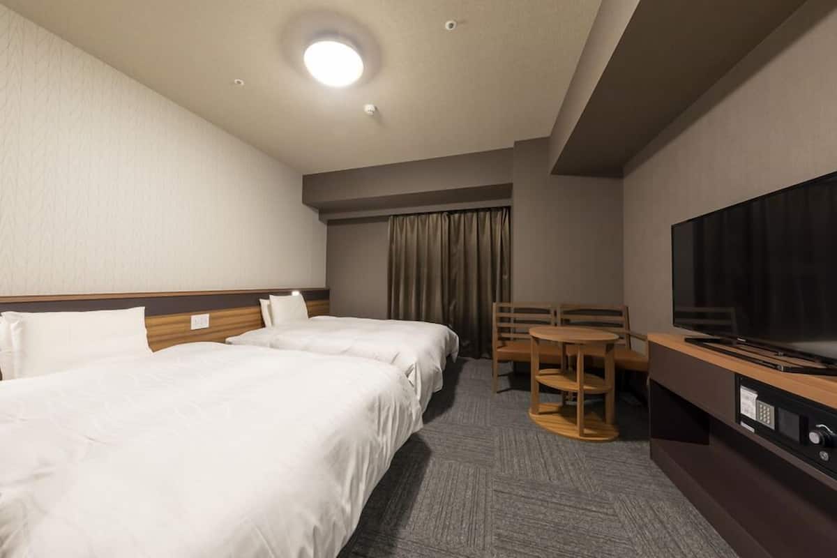 A hotel room with two beds, a TV, a desk, and a chair.
