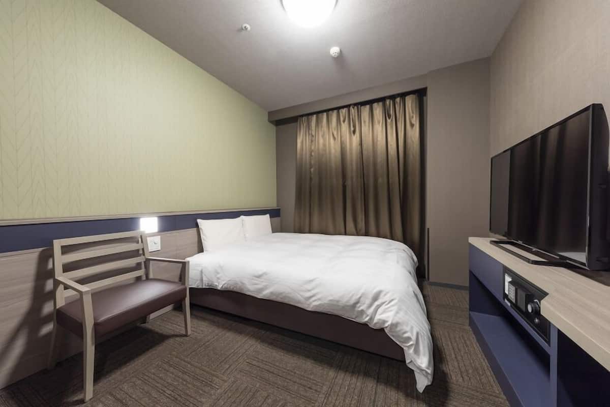 A hotel room with a bed, a bench, a television, and a window with curtains.