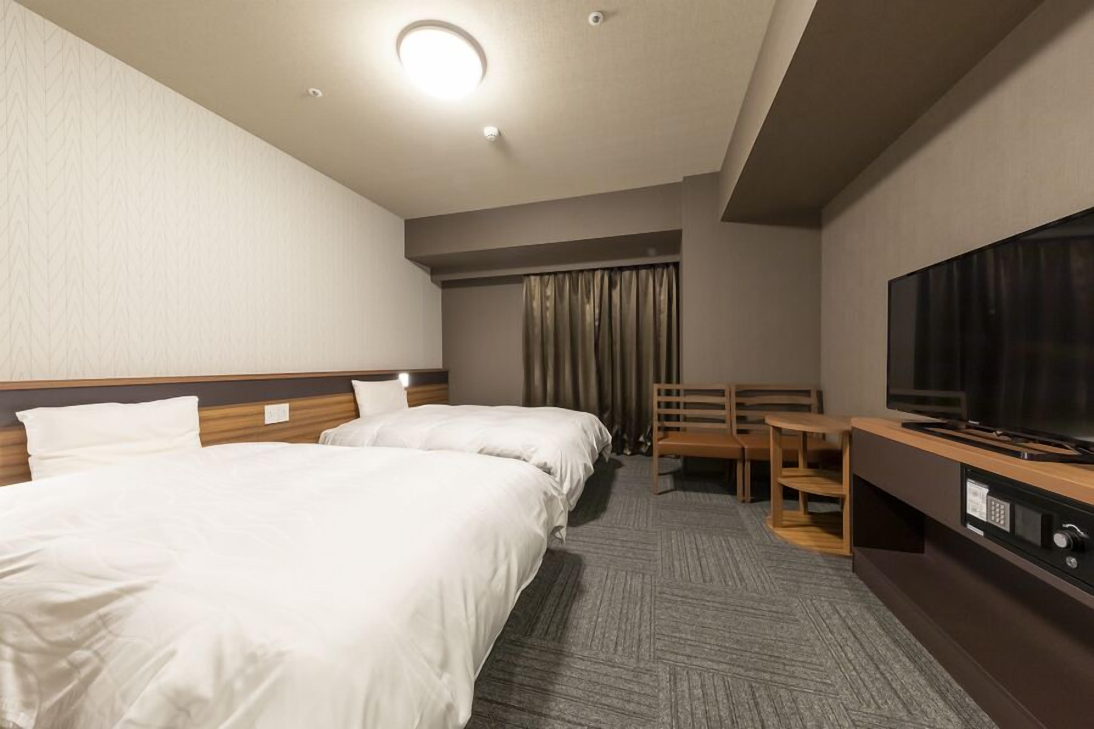 Une chambre d’hôtel avec deux lits, une télévision, un bureau et une chaise.