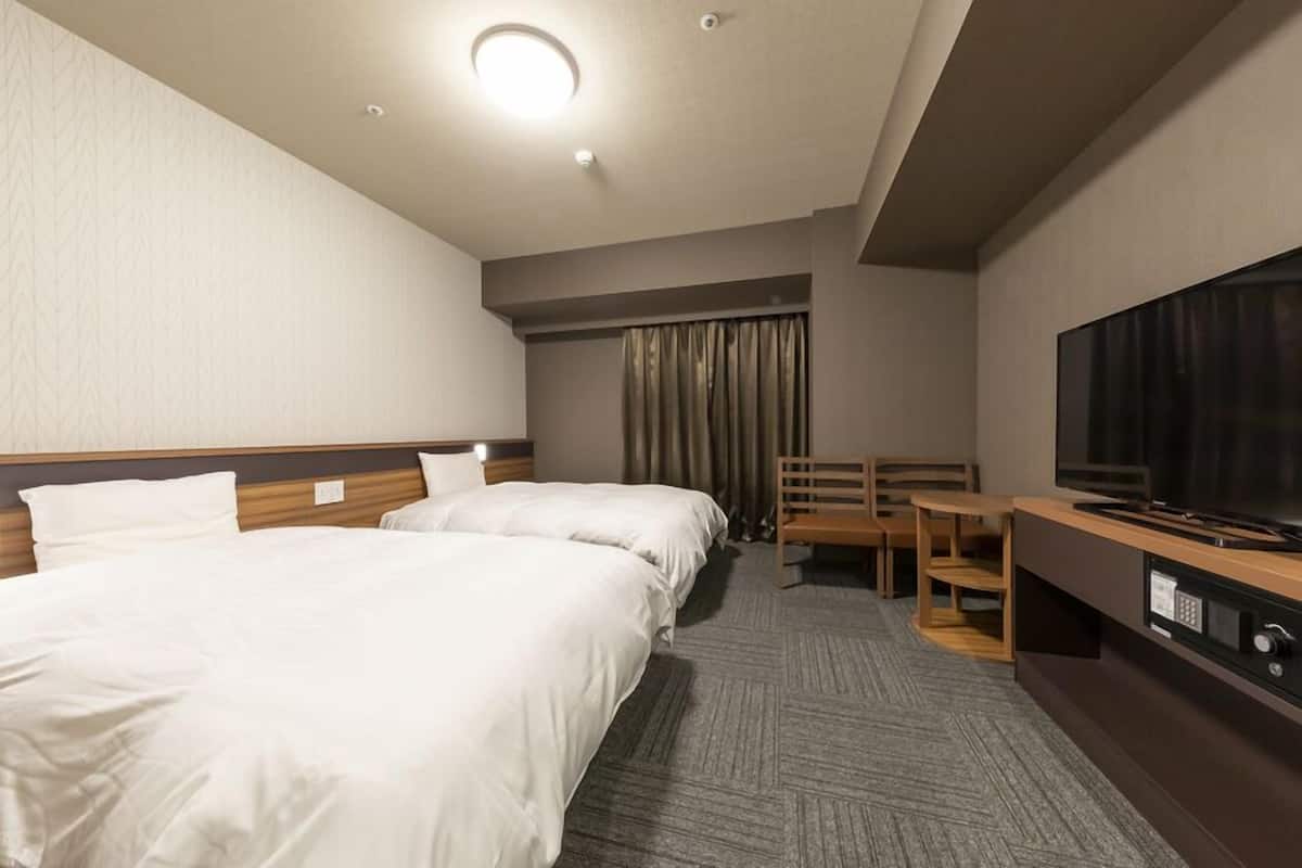 A hotel room with two beds, a television, a desk, and a chair.