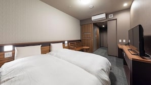 A hotel room with a large bed, a desk with a television, a small table, and an air conditioning unit.