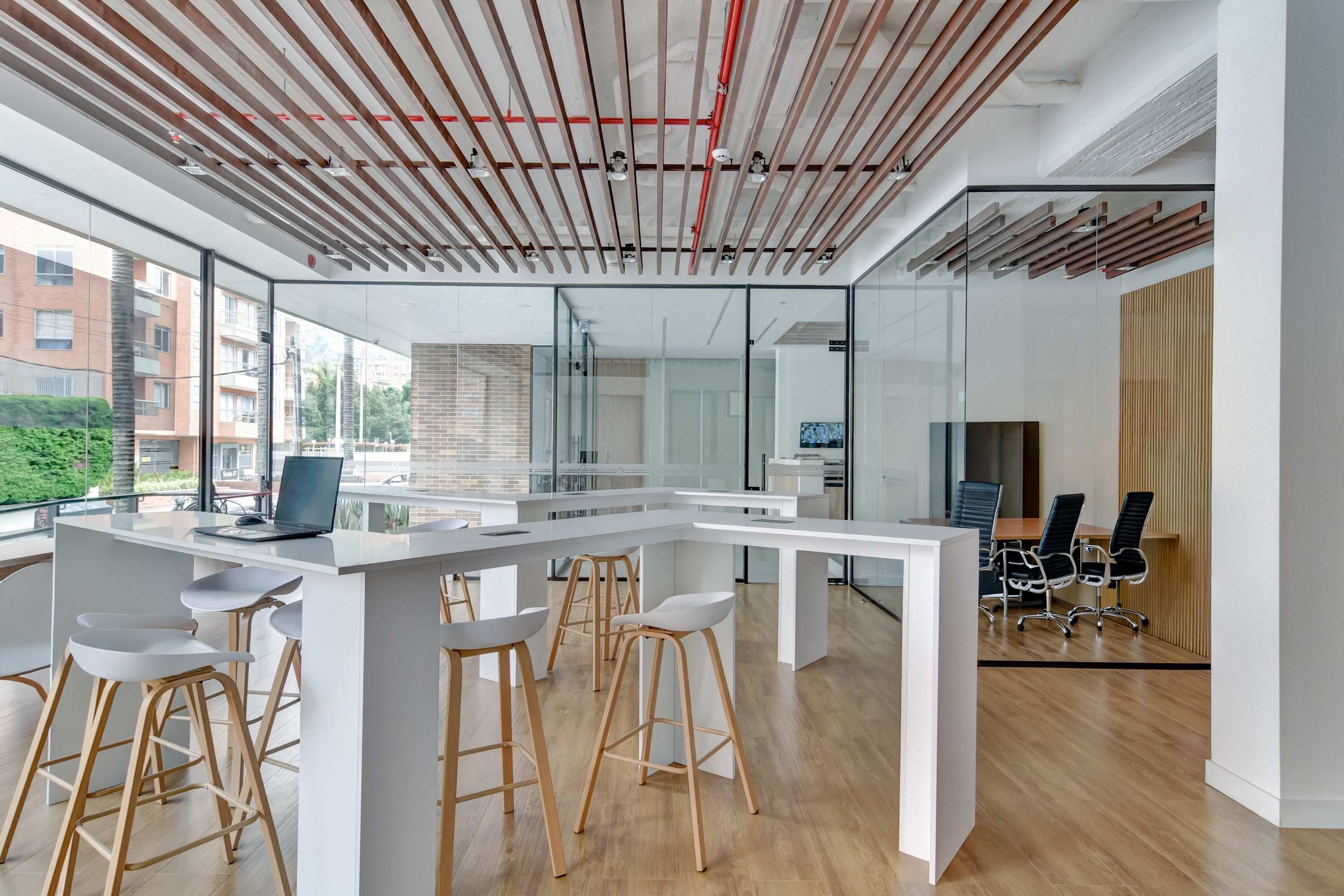 A modern office space with a white desk, bar stools, a laptop, and a conference area with chairs.