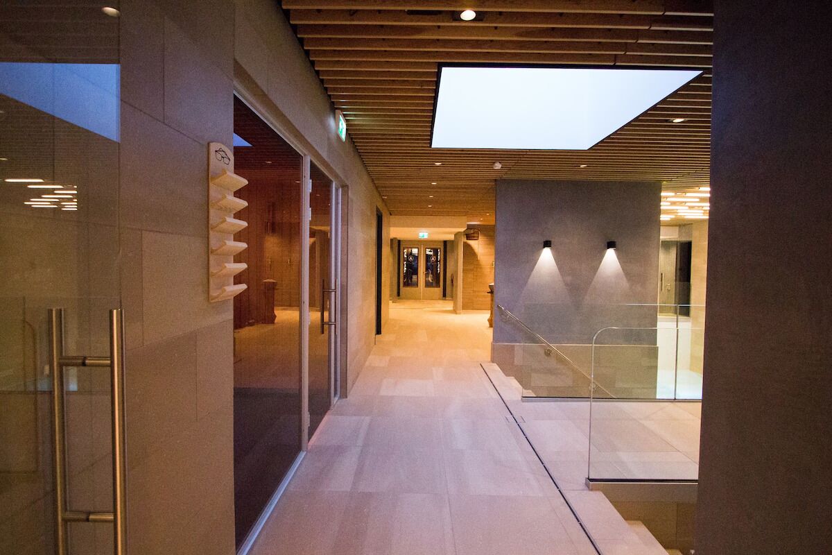 Un corredor moderno de hotel con puertas de vidrio, una escalera y un tragaluz.