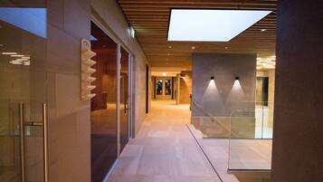 Un corredor moderno de hotel con puertas de vidrio, una escalera y un tragaluz.