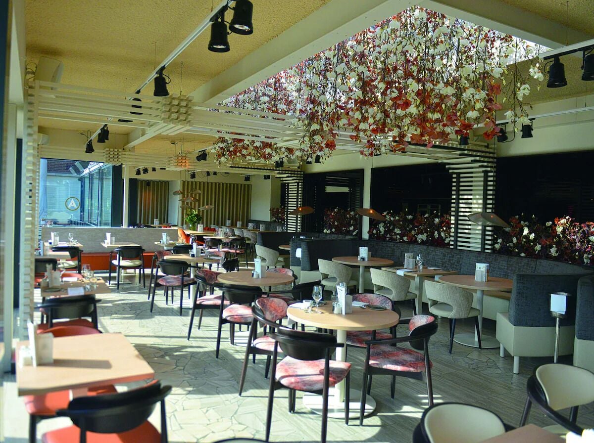 An indoor dining area with tables and chairs, a ceiling with hanging floral decorations, and a view of the outside through large windows.