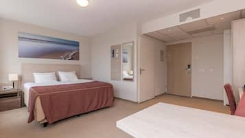 A hotel room with a bed, bedside table, lamp, and a painting of a beach scene.