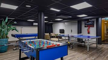 Een kamer met een tafelvoetbaltafel, een pingpongtafel en een grote potplant.