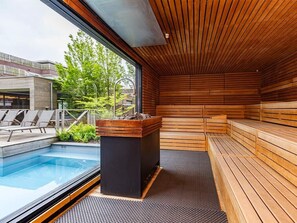 Een moderne, binnensauna met houten banken, een klein zwembad en uitzicht op buiten.