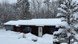 A snow-covered cabin with a front door, windows, and a small porch area.