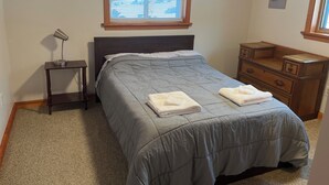 A bedroom with a bed, a nightstand, a dresser, a window with blinds, and a lamp.