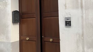 Une porte en bois à deux battants, surmontée d’une arche vitrée, avec une boîte aux lettres et une caméra de surveillance fixée au mur.