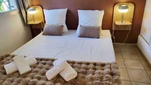 Ein Hotelzimmer mit einem großen Bett, zwei Nachttischlampen, einer weichen braunen Tagesdecke und zwei aufgerollten Handtüchern.