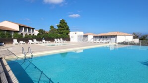 Ein klares, blaues Schwimmbecken mit Holzterrasse und Liegestühlen, umgeben von Gebäuden und Bäumen.