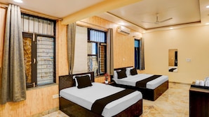 Une chambre d’hôtel avec deux lits, un ventilateur de plafond, un appareil de climatisation et un petit bureau équipé de produits de toilette.