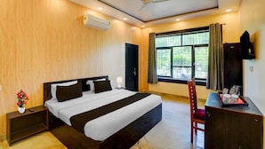 Une chambre d’hôtel équipée d’un lit, d’un bureau, d’une chaise, d’un ventilateur de plafond et d’une fenêtre avec des rideaux.