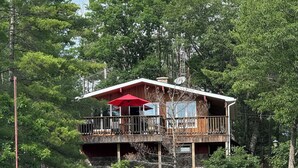 A wooden cabin with a balcony, a red umbrella, and a dock with a boat. - Peaceful Kawartha Lakes Cottage | Kayak, SUP & Stunning Sunsets (North Kawartha)