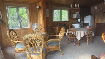 A wooden cabin interior with wicker furniture, a dining table, and a kitchen area.