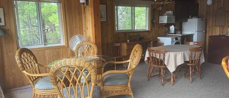 A wooden cabin interior with wicker furniture, a dining table, and a kitchen area.