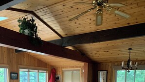 A cozy cabin interior with a wooden ceiling, a sofa, dining table, chairs, and a ceiling fan. - Peaceful Kawartha Lakes Cottage | Kayak, SUP & Stunning Sunsets (North Kawartha)