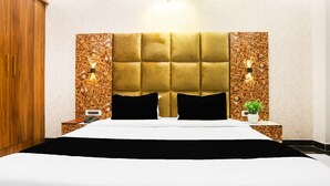 A hotel room with a large bed, a wooden wardrobe, a nightstand with a phone, and a wall-mounted light fixture. - Townhouse Kota Airport (Kota)