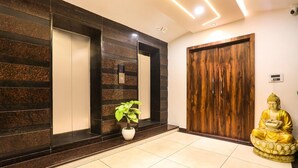 A reception area with a potted plant, a Buddha statue, a wooden door, and a wall with a vertical stripe pattern. - Townhouse Kota Airport (Kota)
