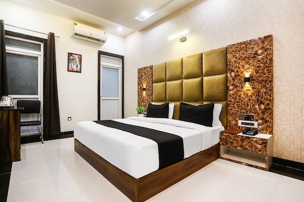 A modern hotel room with a large bed, a bedside table, a wall-mounted air conditioner, and a door with curtains.
