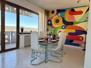 A dining area with a glass table, white chairs, and a colorful abstract wall. - 160 sqm apartment with a spectacular 180° view of Verona (Verona)