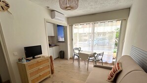 A living room with a sofa, TV, wooden dresser, and a dining area with chairs and a table. - Beachfront studio, AC - 2 guests (Argelès-sur-Mer)