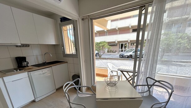 A compact kitchen with a coffee maker, a sink, and a window. There is a dining table with two chairs and a small table with a decorative item. - Beachfront studio, AC - 2 guests (Argelès-sur-Mer)