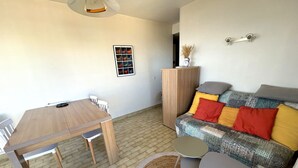 A living area with a wooden dining table, a sofa with patterned cushions, a small round table, and a woven rug. - Sea view apartment, private parking - 4 guests (Argelès-sur-Mer)