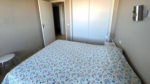 A bedroom with a bed, a chair, a wardrobe, and a door leading to another room. - Sea view apartment, private parking - 4 guests (Argelès-sur-Mer)
