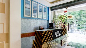 A reception desk with a 'HOTEL' sign, framed artwork on the wall, and a view of greenery outside. - Deluxe Easy Stay (Bhopal)