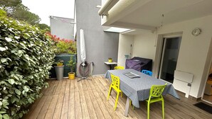 Un patio con terraza de madera, una mesa con mantel estampado, sillas amarillas y una parrilla cubierta.