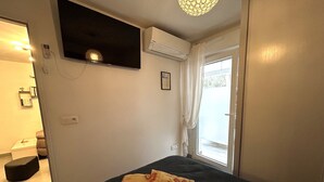 Un dormitorio con cama, televisor montado, equipo de aire acondicionado, ventana con cortinas y puerta.