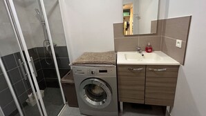 Un baño pequeño con cabina de ducha de vidrio, lavadora y lavabo con espejo.
