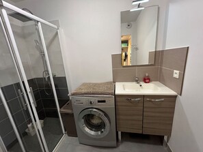 A compact bathroom with a glass shower enclosure, a washing machine, and a sink with a mirror above it. - Apartment with AC and parking - 4 guests (Argelès-sur-Mer)